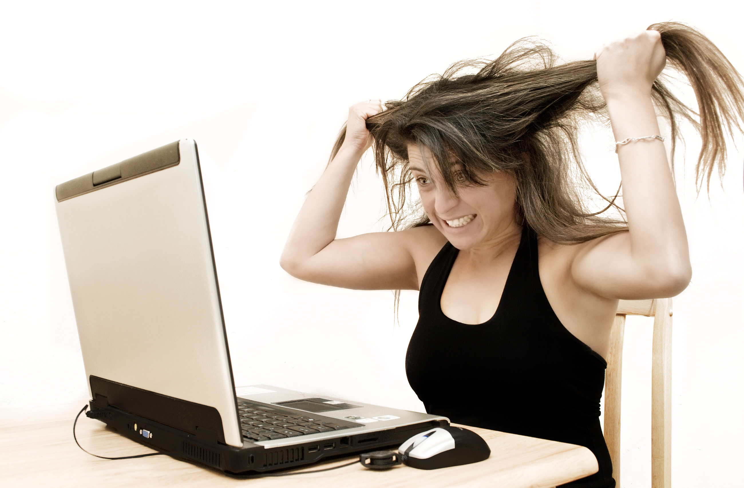 A woman expresses fury whilst looking at her laptop.