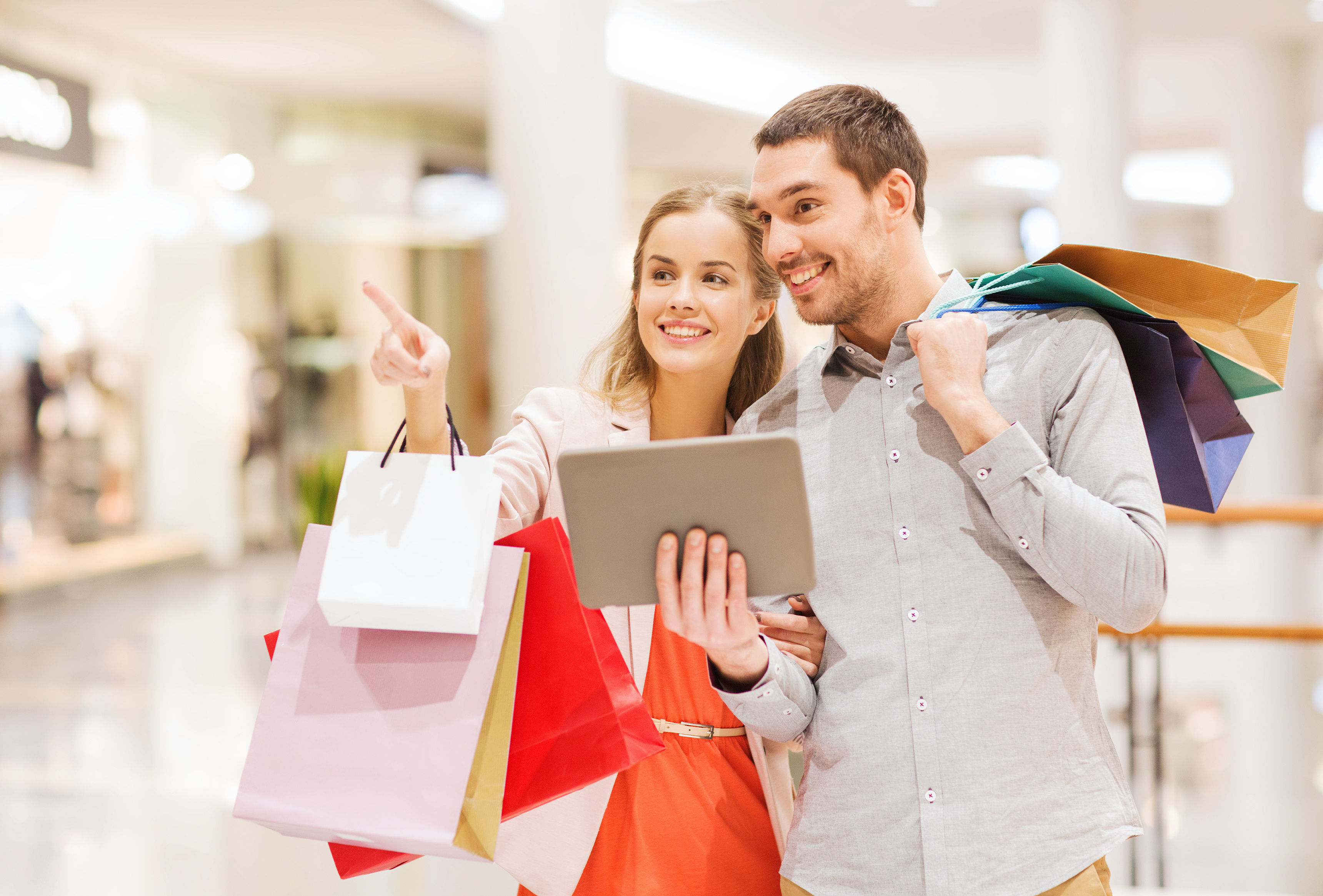 couple with tablet pc and shopping bags in mall